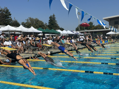 Swimmers dive into the pool during the girls 15-18 200-yard medley relay.