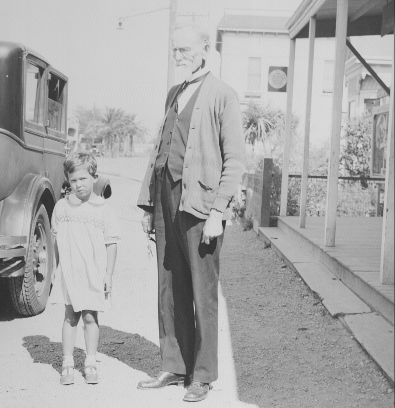 Albert Norris Senior and his grandchild stand in front of the Alvarado Library.  The County Free library stood at today’s Smith Street and Vallejo Street. The building is now gone, replaced by the Old Alvarado Public Parking Plaza. The Alameda County Free Library logo can be seen on the building. (Alvarado)