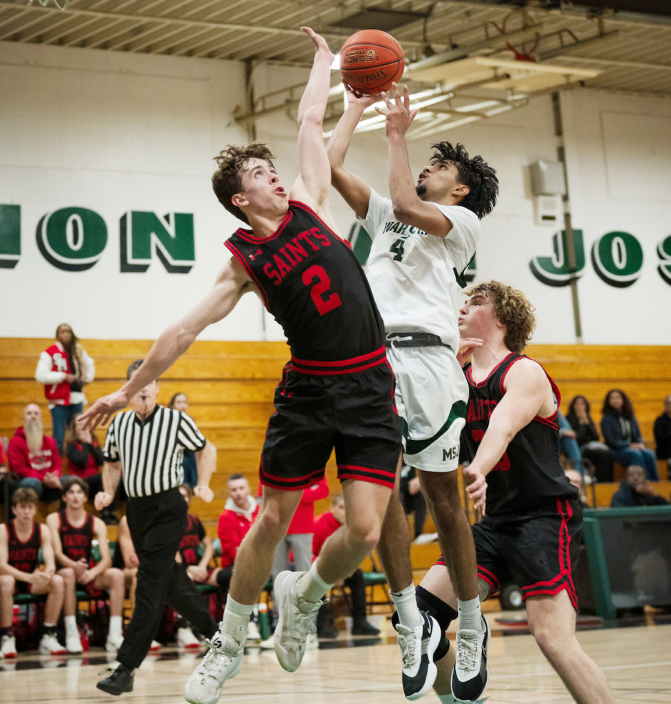 Warriors’ forward Ankit Srinivas, shoots over the outstretched arm of Saints’ guard Peter Oliver. Photo by Agnes White