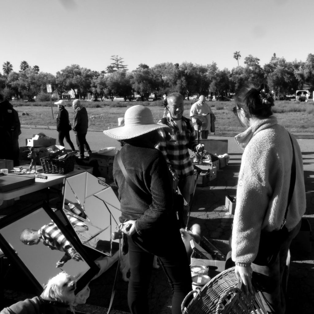 At the Ohlone College Flea Market, big hats are discussed; dog owners chat over baskets and their reflection.